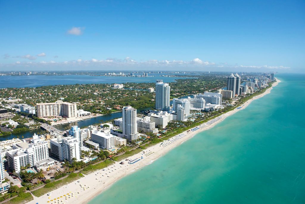 Aerial view of Miami Beach coastline with turquoise ocean and high-rise hotels.