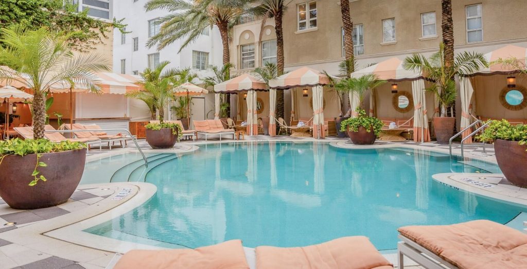 The Plymouth South Beach pool with palm trees and striped cabanas.