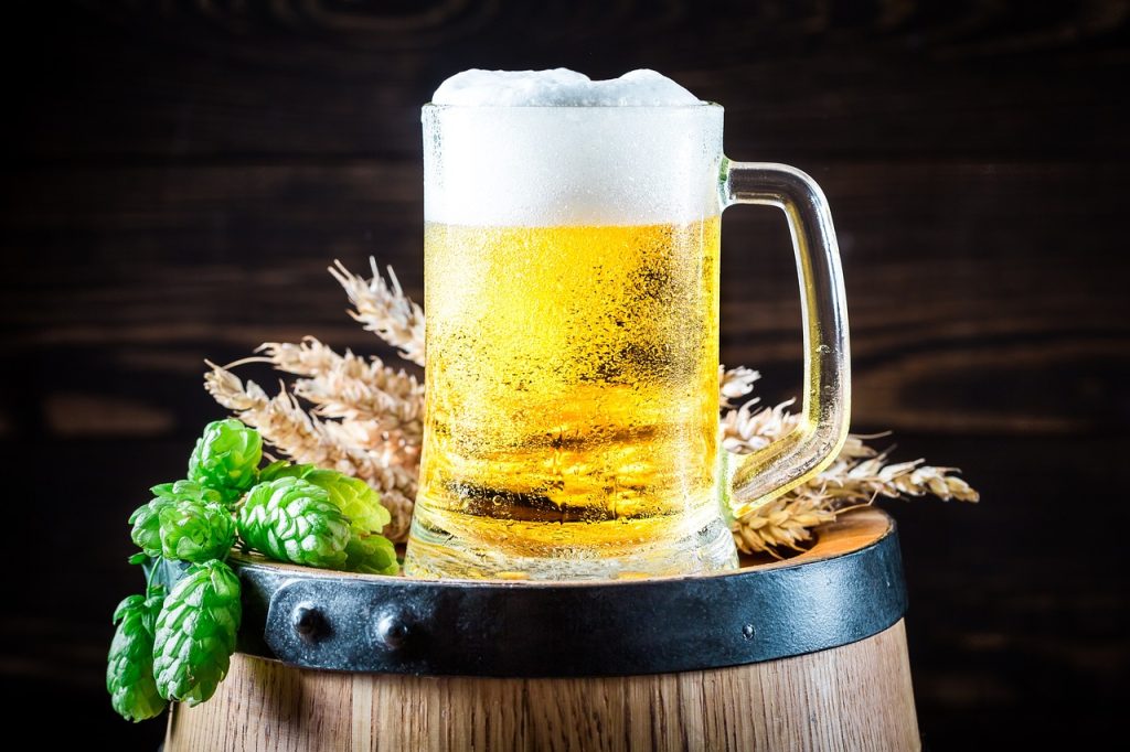 Glass mug of golden beer with foam on a wooden barrel